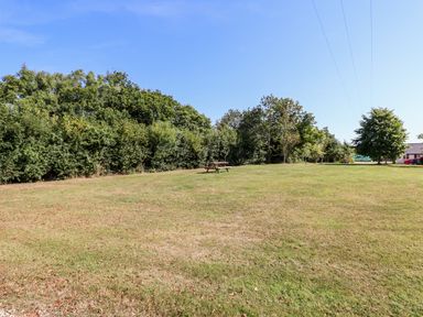 A large grassy open area with a wooden picnic table surrounded by trees and a house in the background at Little Rowan at Rowan Park Farm in Ashwater