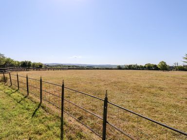 A fenced grassy field with trees and hills in the background at Little Rowan at Rowan Park Farm in Ashwater