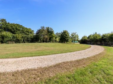 A gravel path curving through a grassy area with trees and a picnic bench at Little Rowan at Rowan Park Farm in Ashwater