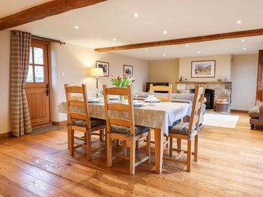 A dining table with six chairs and a flower vase in a room with a stone fireplace and wooden beams at Little Orchard in Ashburton Down near Ashburton