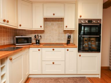 A kitchen with white cabinets wooden countertops a microwave oven built-in oven utensils and a knife block at Little Orchard in Ashburton Down near Ashburton