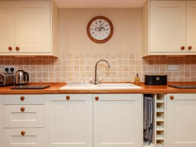 A kitchen with cream cabinets a wooden countertop a sink a wall clock and small appliances at Little Orchard in Ashburton Down near Ashburton