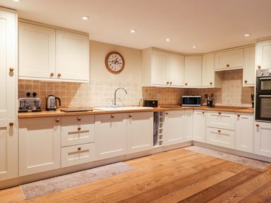 A kitchen with white cabinets wooden countertops and wood flooring at Little Orchard in Ashburton Down near Ashburton