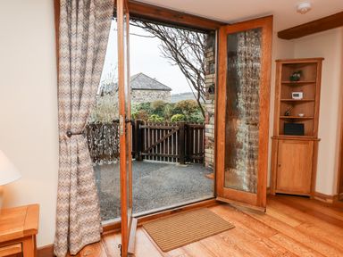 A room with an open glass door leading outside and wooden furniture at Little Orchard in Ashburton Down near Ashburton