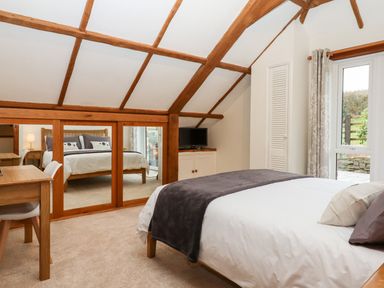 A bedroom with a bed, desk, chair, TV, mirrored wardrobes and window at Little Orchard in Ashburton Down near Ashburton