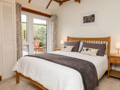 A bedroom with a wooden bed frame bedside tables lamps and glass doors leading outside at Little Orchard in Ashburton Down near Ashburton