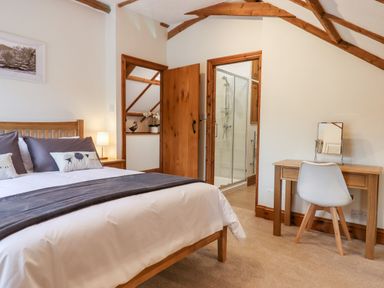 A bedroom with a wooden bed beside a nightstand lamp and a desk with a chair and mirror at Little Orchard in Ashburton Down near Ashburton