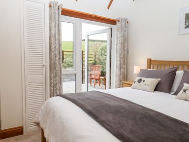 A bedroom with a wooden bed and cushions next to glass doors leading to a patio at Little Orchard in Ashburton Down near Ashburton