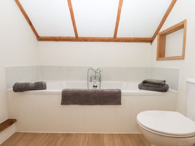 A bathroom with a bathtub with gray towels and a toilet at Little Orchard in Ashburton Down near Ashburton