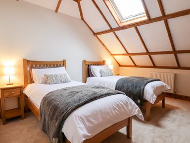 A bedroom with two single beds bedside tables and lamps under a sloped ceiling at Little Orchard in Ashburton Down near Ashburton