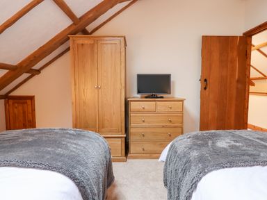 A bedroom with two beds covered in gray blankets wooden wardrobe and chest of drawers with a TV on top at Little Orchard Ashburton Down near Ashburton