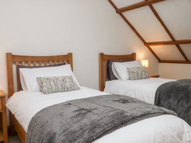 A bedroom with two single wooden beds with white bedding and gray throws at Little Orchard in Ashburton Down near Ashburton
