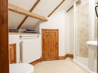 A bathroom with a shower enclosure a sink towels on a shelf and exposed wooden beams at Little Orchard in Ashburton Down near Ashburton