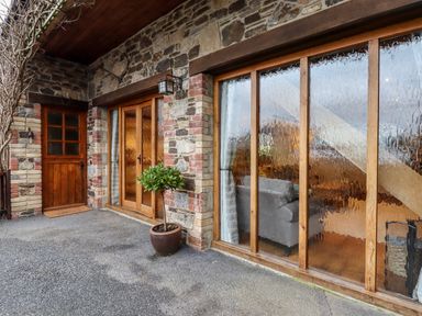 Exterior view of a stone house with wooden door, glass sliding door, and potted plant at Little Orchard Ashburton Down near Ashburton