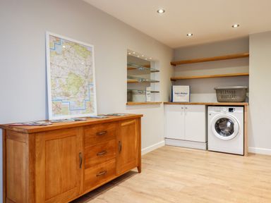 A utility room with a wooden sideboard a washing machine wooden shelves and a framed map at Little Orchard in Ashburton Down near Ashburton