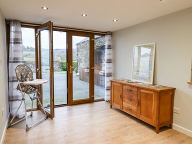 A room with wooden floor and furniture including a high chair and a sideboard with a framed map at Little Orchard Ashburton Down near Ashburton