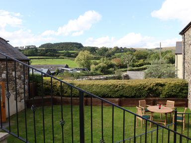 A backyard with a round table and four chairs on grass bordered by hedges and stone buildings at Little Orchard in Ashburton Down near Ashburton