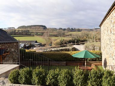 A garden with green bushes a patio table with a green umbrella stone buildings and fields at Little Orchard Ashburton Down near Ashburton