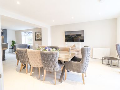 A dining area with a rectangular table and upholstered chairs next to a wall-mounted television at Aelfor in Harlech