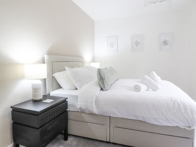 A bedroom with a bed with white bedding two pillows and three rolled towels a black nightstand with a lamp and three framed pictures on the wall at Aelfor in Harlech