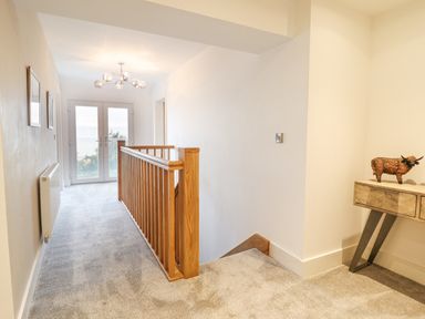 A carpeted upstairs hallway with wooden banisters and double glass doors at Aelfor in Harlech
