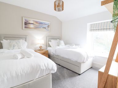 A bedroom with two single beds white bedding a nightstand with a lamp and a window with striped blinds at Aelfor in Harlech