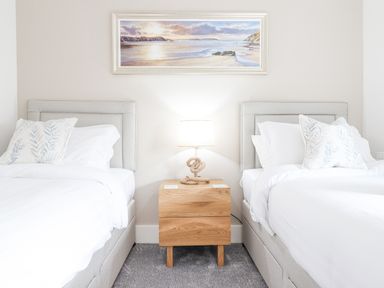A bedroom with two single beds separated by a wooden nightstand with a lamp and a painting above at Aelfor in Harlech