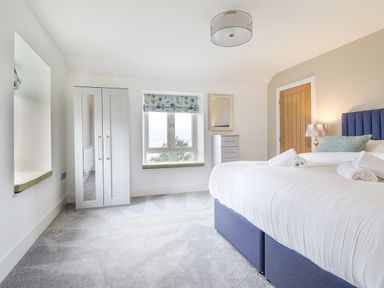 A bedroom with a bed and rolled towels next to a window with floral blinds at Aelfor in Harlech