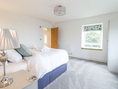 A bedroom with a bed, bedside table with lamp, window, and an open door at Aelfor in Harlech