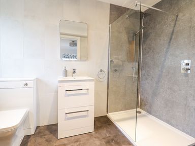 A bathroom with a toilet, sink with cabinet, mirror, and walk-in shower at Aelfor in Harlech