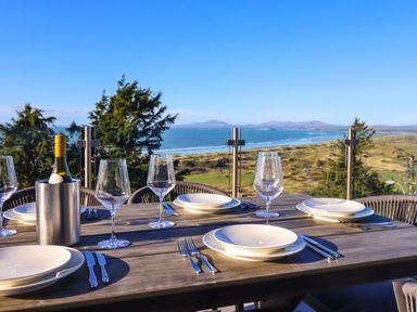An outdoor dining table set with plates wine glasses cutlery and a bottle of wine overlooking a coastal landscape at Aelfor in Harlech