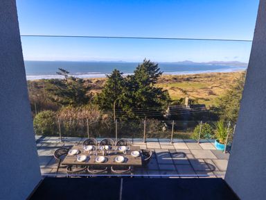 An outdoor dining table set for eight on a balcony overlooking trees sand dunes and the ocean at Aelfor in Harlech