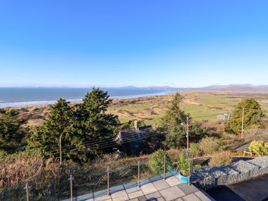 A coastal landscape with trees a grassy area and a paved terrace with a potted plant at Aelfor in Harlech
