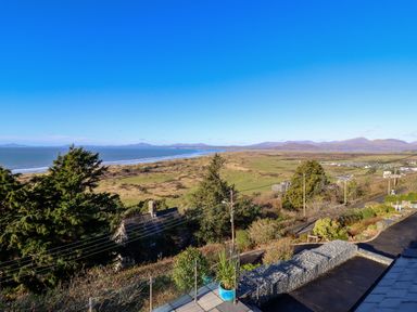A coastal landscape with a beach and grassy dunes with distant mountains and a small road with houses at Aelfor in Harlech