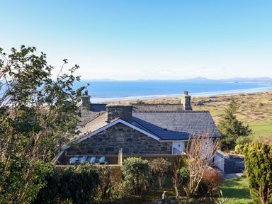 A stone house with chimneys near the sea with hills in the background at Aelfor in Harlech