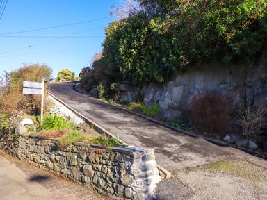 A narrow paved driveway going uphill bordered by a stone wall and vegetation at Aelfor in Harlech