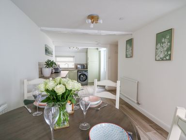 A dining table set with plates glasses and a vase of flowers in a room with a kitchen in the background at 2 Penporth in Rhayader