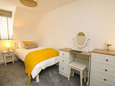 A bedroom with a single bed yellow bedspread and a vanity table with a mirror at 2 Penporth in Rhayader