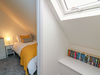 A bedroom with a single bed linens and pillows next to a bedside table and lamp and a shelf with books under a skylight at 2 Penporth in Rhayader