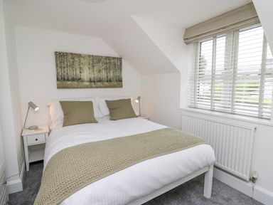 A bedroom with a bed pillows bedside tables lamps and window blinds at 2 Penporth in Rhayader