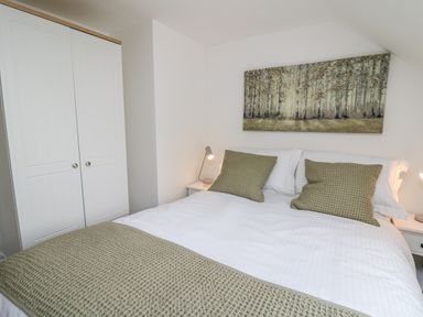 A bedroom with a double bed with green cushions and blanket a white wardrobe and bedside table with lamps at 2 Penporth in Rhayader
