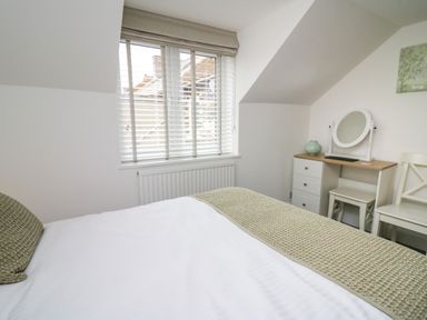 A bedroom with a bed pillow and blanket near a window with blinds and a dressing table with a mirror and chair at 2 Penporth in Rhayader