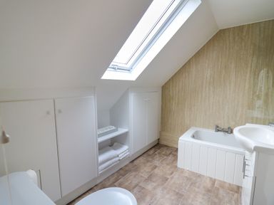 A bathroom with a bathtub a sink a toilet and storage cabinets under a skylight at 2 Penporth in Rhayader