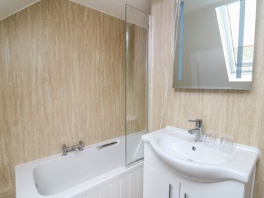 A bathroom with a bathtub a glass shower screen a sink with a faucet and two glasses at 2 Penporth in Rhayader