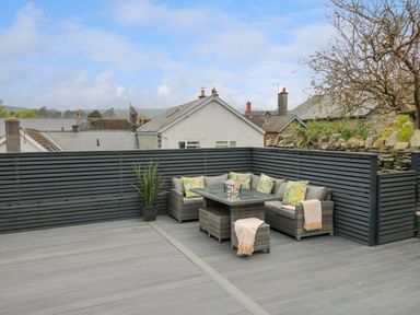 An outdoor patio with gray wooden decking a corner sofa set with a glass table cushions and a plant pot at 2 Penporth in Rhayader