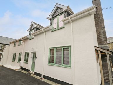 A white two-story house with green window frames and a green door at 2 Penporth in Rhayader