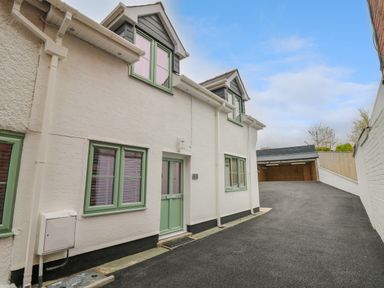 A white residential building with green window frames and doors next to a driveway leading to a carport at 2 Penporth in Rhayader