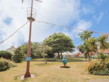 A park area with a tall metal pole, string lights, greenery, a painted bird sculpture and houses in the background at Bluebell Cottage in Flamborough