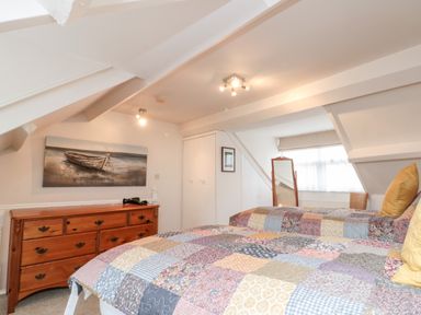 A bedroom with two single beds with patchwork quilts a wooden dresser a standing mirror and a painting of a boat on the wall at Bluebell Cottage in Flamborough