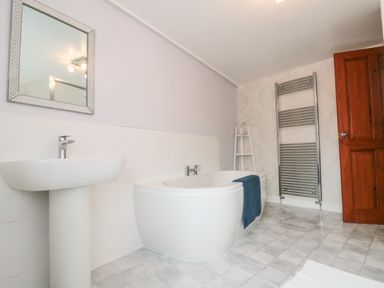 A bathroom with a pedestal sink a bathtub with a blue towel a metal towel rack and a wooden door at Bluebell Cottage in Flamborough